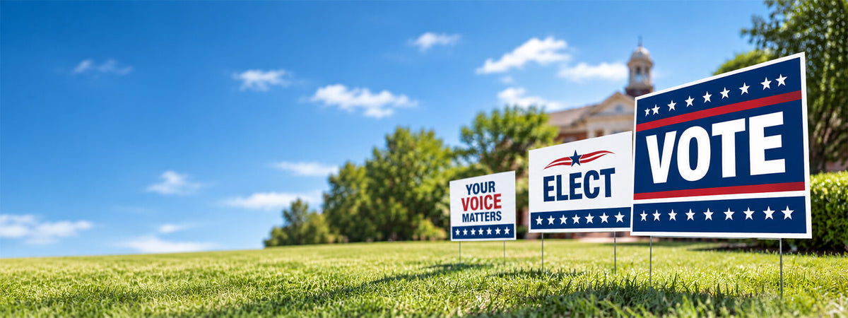 Political campaign yard signs displayed on a green lawn, including red, white and blue signs for voting and elections.